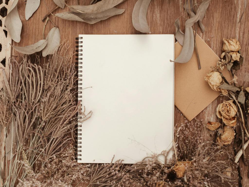 A blank notebook surrounded by dried flowers offers a rustic, creative background.
