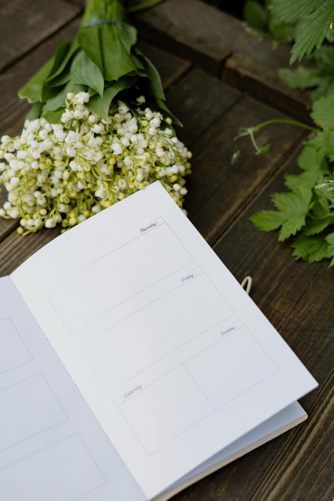 Elegant lily of the valley flowers next to an open planner on a rustic wooden surface, perfect for lifestyle themes.