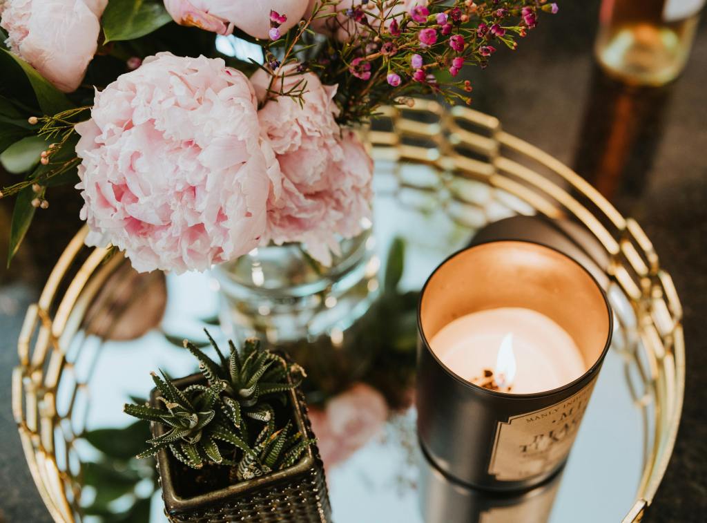 A close-up of a floral arrangement with a lit candle on a mirrored tray, exuding warmth and elegance.